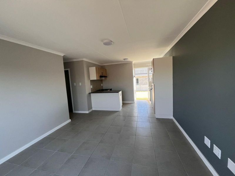 Open plan living area featuring tiled flooring, neutral wall tones, and a compact kitchen with built-in cabinetry and a hob.