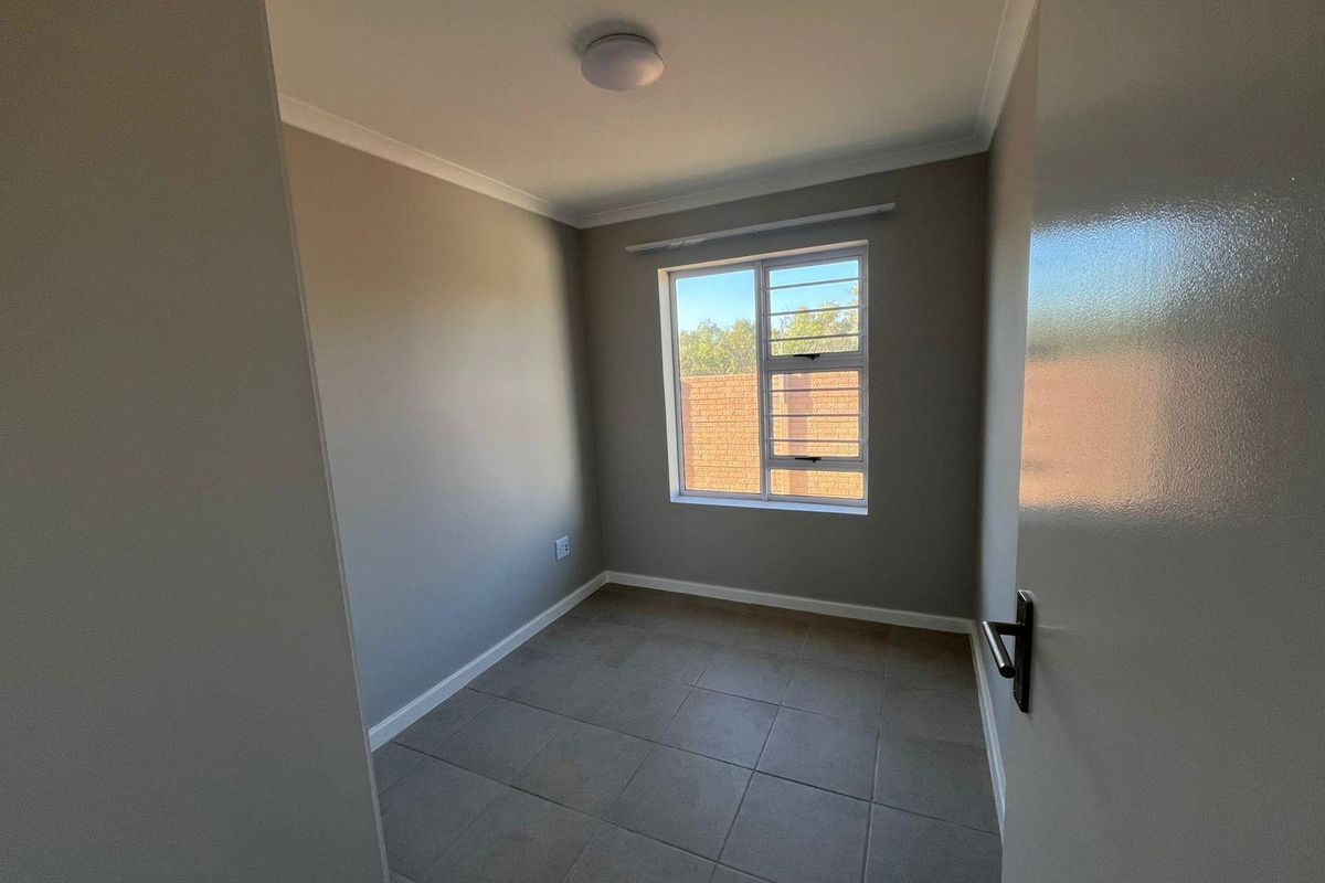 A clean, empty bedroom featuring neutral grey walls, tiled flooring, and a window with security bars.