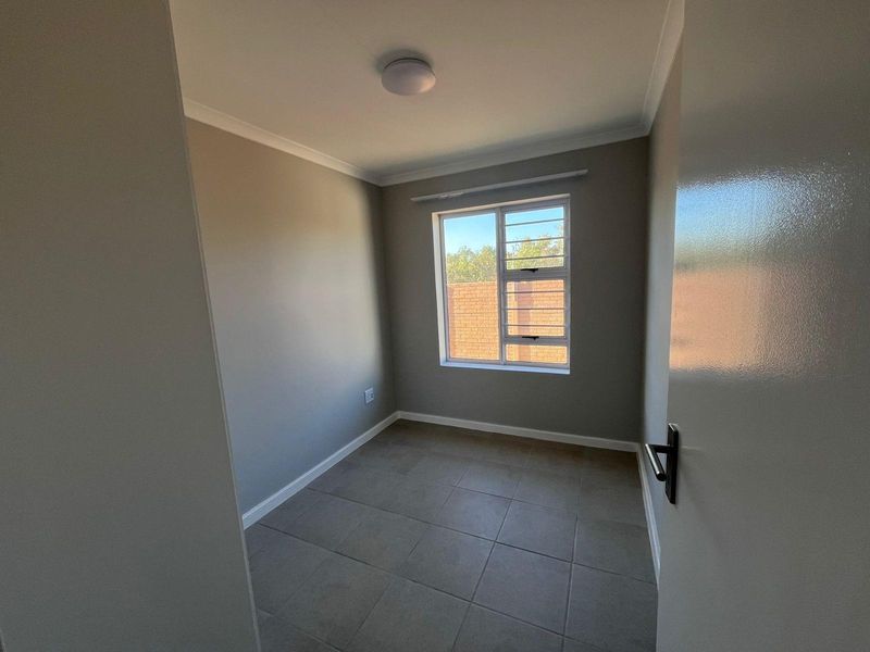 A clean, empty bedroom featuring neutral grey walls, tiled flooring, and a window with security bars.