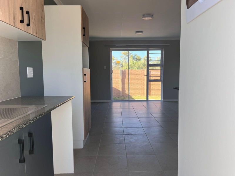 An open-plan kitchen and living area featuring modern cabinetry, tiled flooring, and a sliding glass door leading to the rear outdoor space.