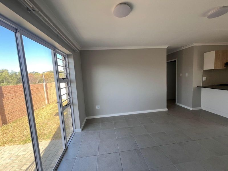 An open-plan living area featuring neutral tiled flooring, modern grey walls, and large sliding glass doors providing access to the outdoor space.