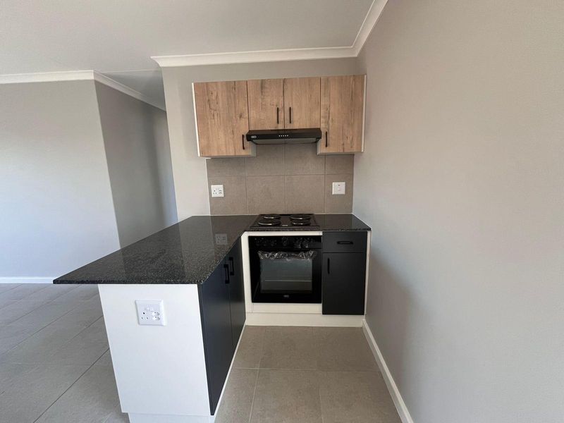 Modern compact kitchen featuring dark cabinetry, granite countertops, built-in oven, electric hob, and extractor fan with neutral tiled flooring.