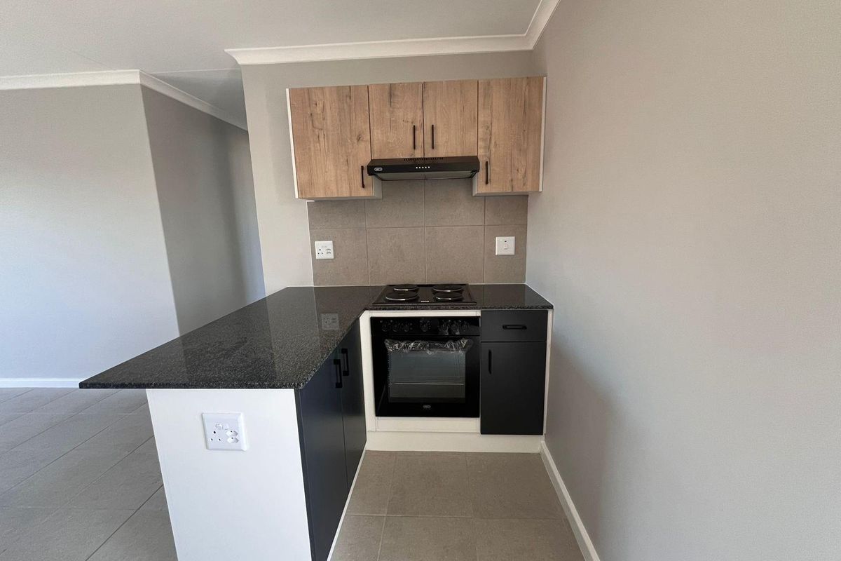Modern compact kitchen featuring dark cabinetry, granite countertops, built-in oven, electric hob, and extractor fan with neutral tiled flooring.