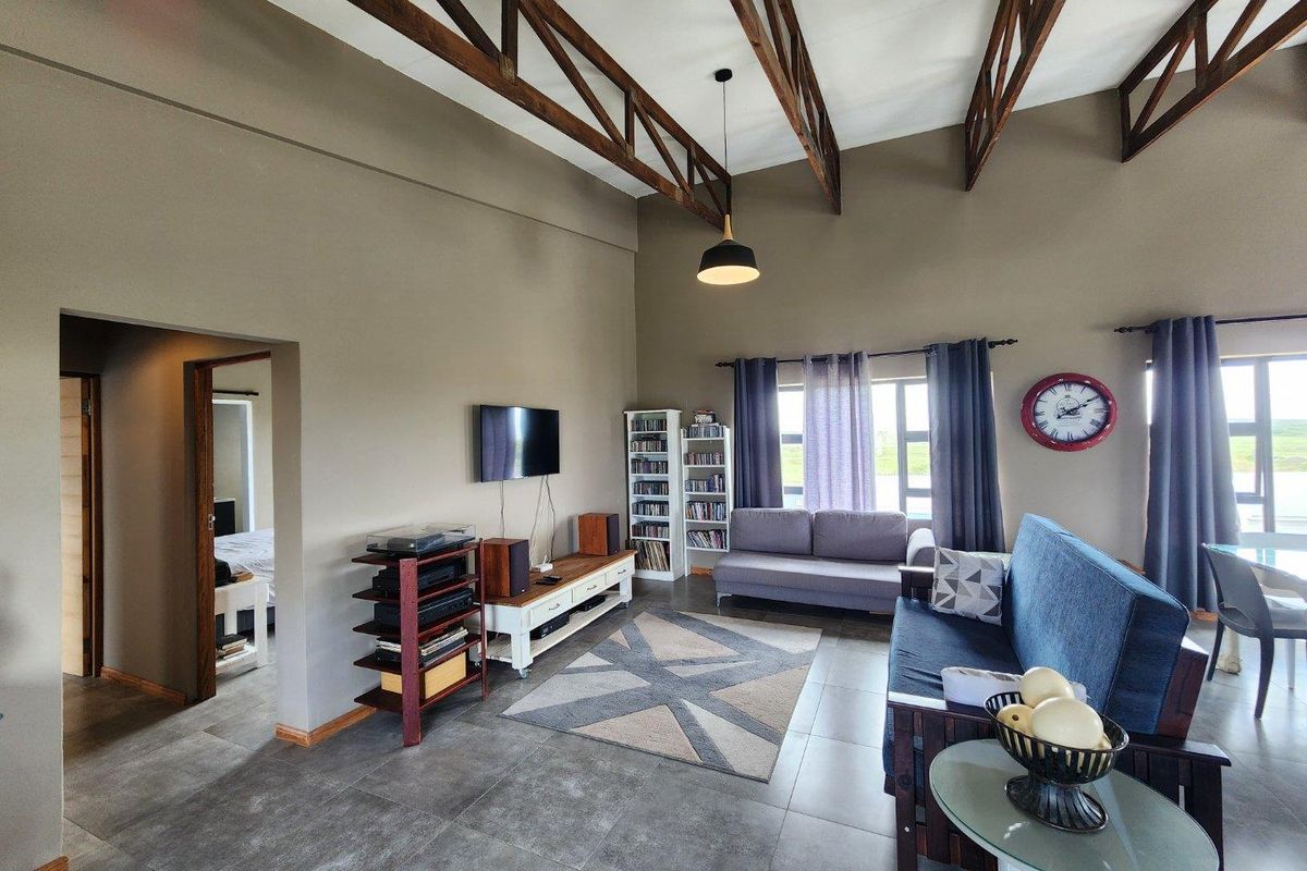Spacious living room featuring high vaulted ceilings with exposed timber trusses, large windows, and modern tiled flooring.