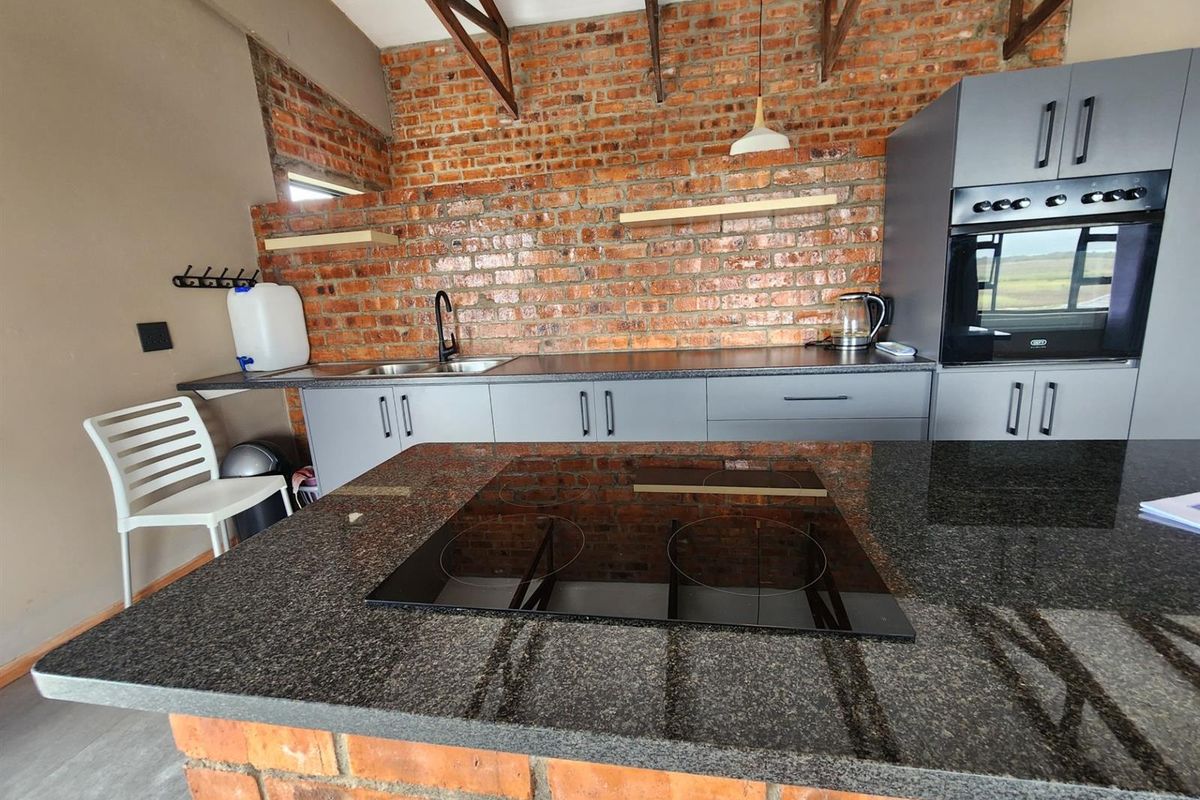 Modern kitchen featuring an exposed brick wall, granite countertops, a central island with a built-in hob, and sleek grey cabinetry with an integrated oven.