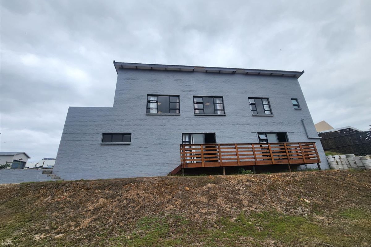 Rear exterior view of a multi-story grey painted brick house featuring a timber deck and multiple window openings.