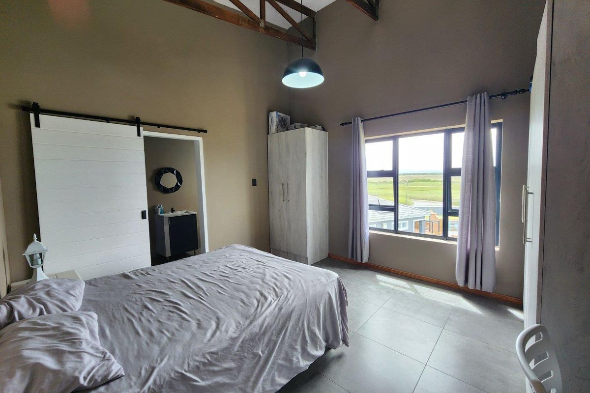Spacious bedroom featuring high vaulted ceilings with exposed timber trusses, large windows with natural light, and an en-suite bathroom accessed via a sliding barn door.