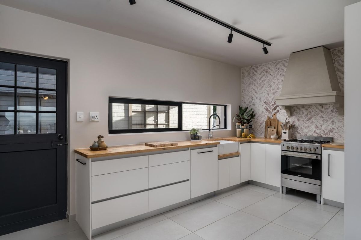 Modern kitchen featuring white cabinetry, timber countertops, a farmhouse sink, a gas range with a custom hood, and a herringbone tiled backsplash.