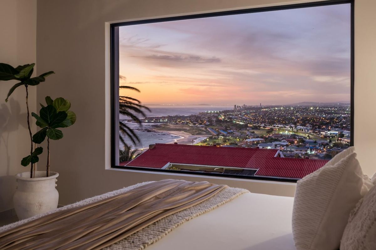 A bedroom featuring a large picture window that frames a stunning panoramic coastal and city sunset view.