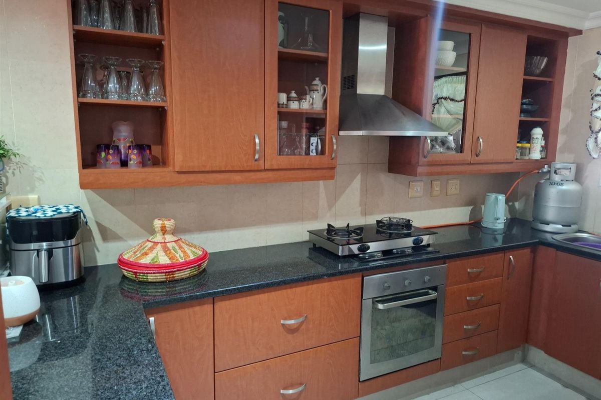 A functional kitchen featuring wooden cabinetry, granite countertops, a built-in oven, gas hob, and stainless steel extractor fan.