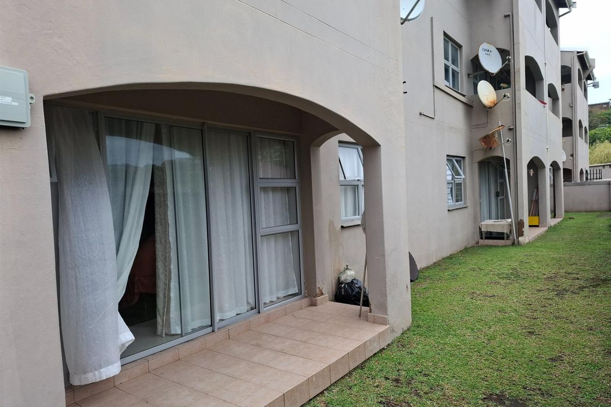 Ground floor apartment exterior featuring a tiled patio area with sliding glass doors and access to a communal garden space.