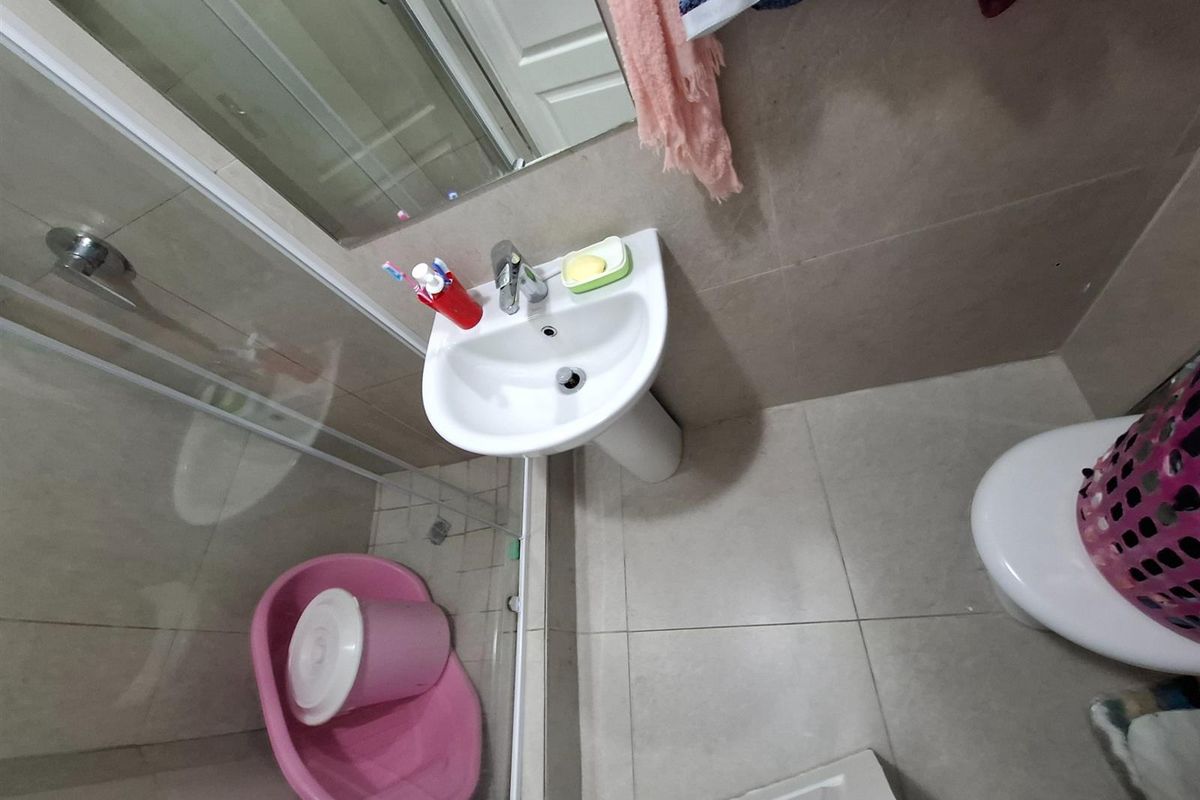 Compact bathroom featuring a pedestal sink, glass-enclosed shower, and tiled flooring.