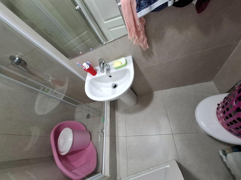Compact bathroom featuring a pedestal sink, glass-enclosed shower, and tiled flooring.