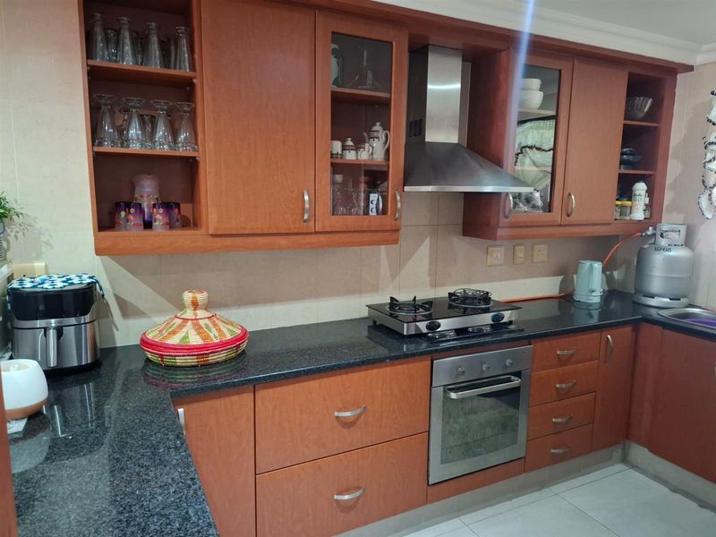 A functional kitchen featuring wooden cabinetry, granite countertops, a built-in oven, gas hob, and stainless steel extractor fan.