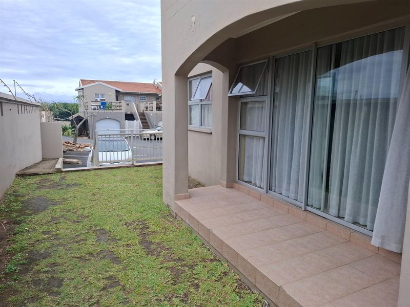 A ground-level patio area with tiled flooring, adjacent to a small private garden space and sliding glass doors leading into the apartment.