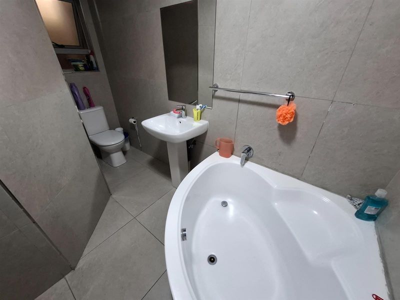 A modern bathroom featuring large-format wall and floor tiles, a corner bathtub, a pedestal basin, and a wall-mounted mirror.