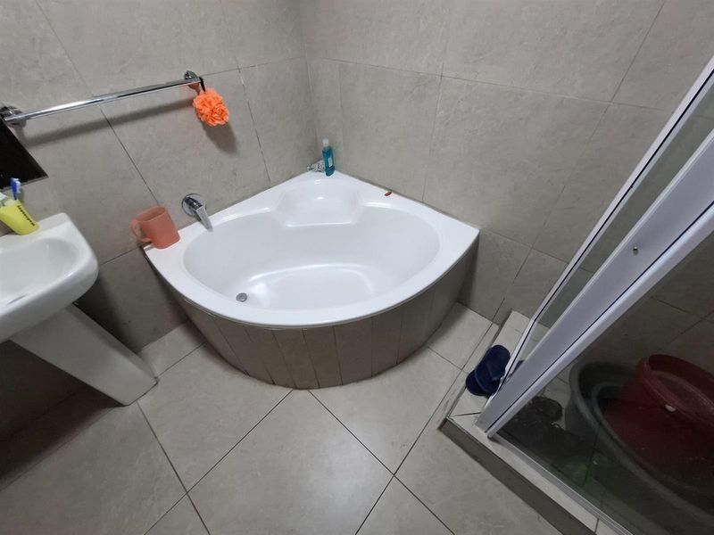 A bathroom featuring a corner bathtub, pedestal basin, and a separate shower enclosure with tiled walls and flooring.