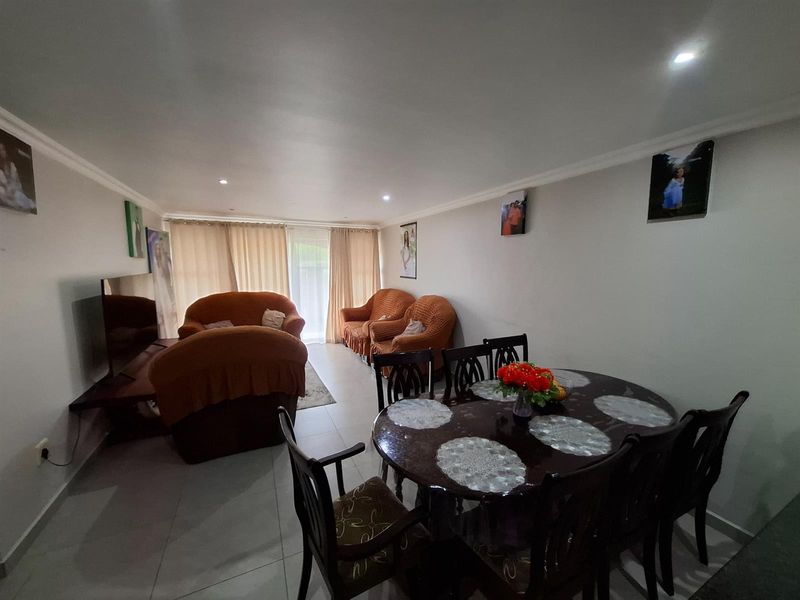 An open-plan living and dining area featuring tiled flooring, recessed ceiling lighting, and large windows with curtains providing natural light.