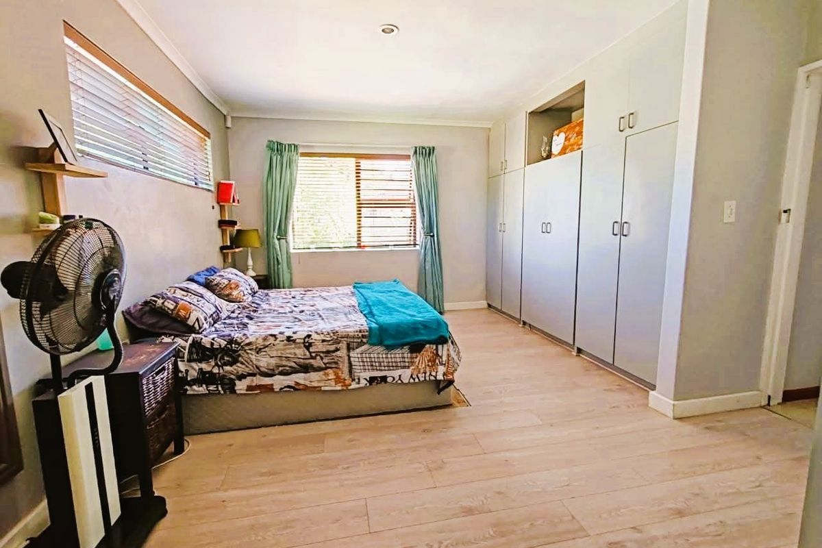 A spacious bedroom featuring light wood-look flooring, built-in floor-to-ceiling cabinetry, and large windows with blinds, offering a clean and functional living space.