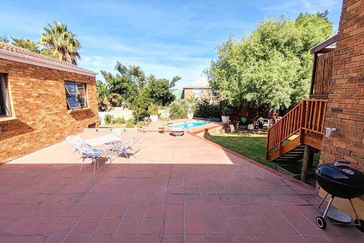 Spacious rear patio area featuring terracotta tiling, a swimming pool, and a wooden staircase leading to the upper level of the house.