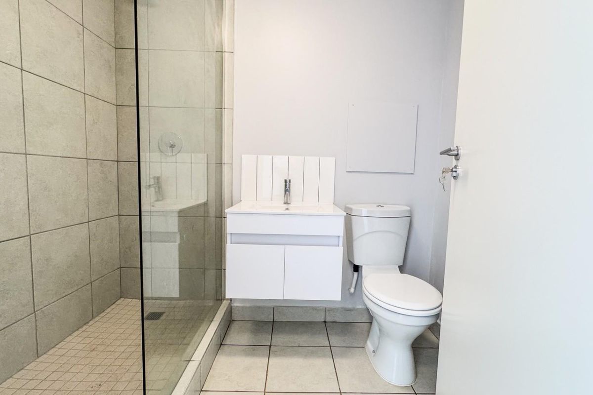 A clean, modern bathroom featuring a glass-enclosed shower, wall-mounted vanity with basin, and a standard toilet with neutral tiled finishes.