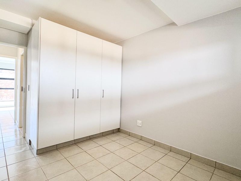 A bright, empty bedroom featuring neutral tiled flooring and clean white built-in cupboards, offering a versatile space ready for personalization.
