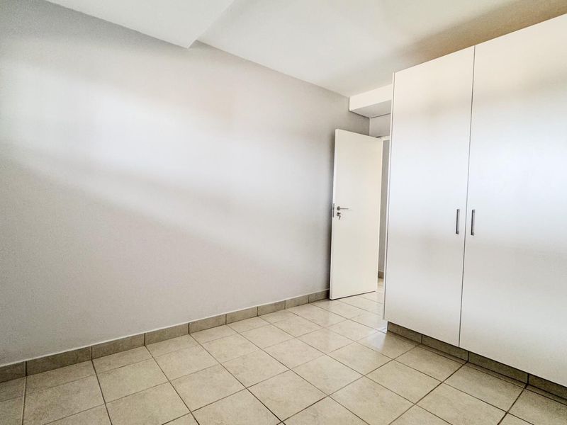 A bright, empty bedroom featuring neutral tiled flooring and a large, modern built-in wardrobe with white cabinetry.
