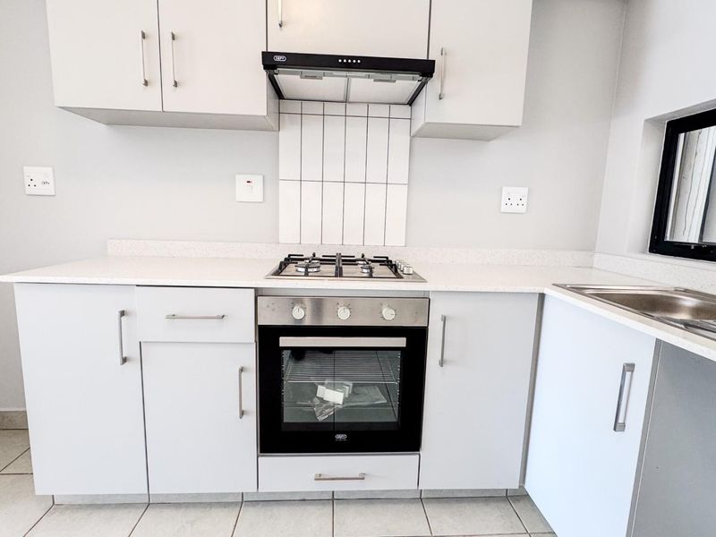 Modern kitchen featuring white cabinetry, stone countertops, a gas hob, built-in oven, extractor fan, and a stainless steel sink with tiled splashback.