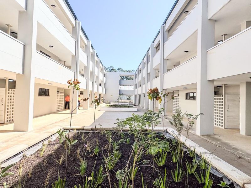 A well-maintained central courtyard area featuring landscaped garden beds, paved walkways, and multi-level apartment building facades with integrated breeze block architectural details.