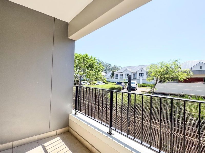 A clean, covered balcony featuring tiled flooring and a secure metal balustrade, offering an open view of the surrounding residential area.