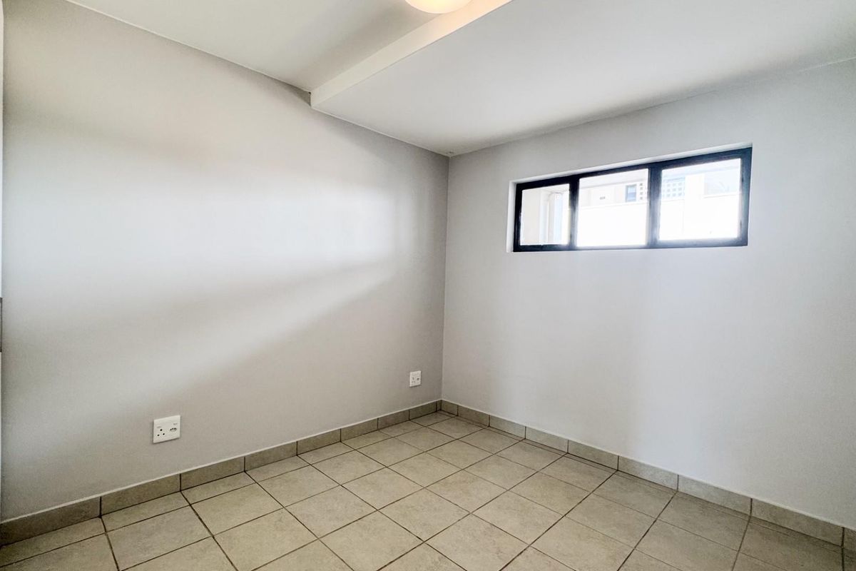 A clean, empty bedroom featuring neutral wall paint, tiled flooring, and a built-in cupboard with modern hardware.