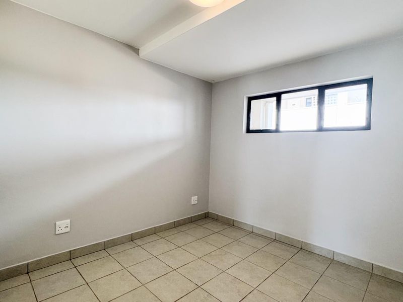 A clean, empty bedroom featuring neutral wall paint, tiled flooring, and a built-in cupboard with modern hardware.