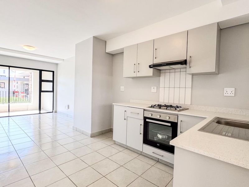 Open-plan kitchen and living area featuring neutral cabinetry, built-in appliances, tiled flooring, and a sliding door leading to an outdoor space.