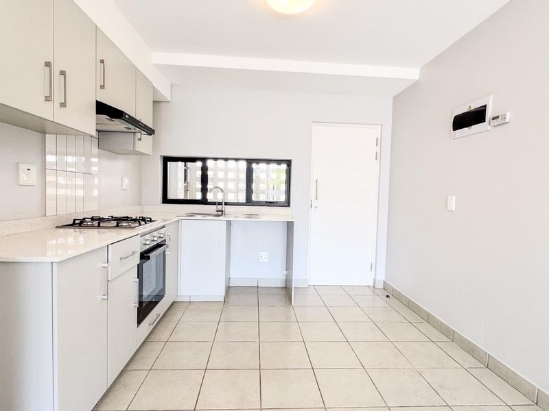 A clean, modern kitchen featuring light-toned cabinetry, a gas hob, built-in oven, and tiled flooring, offering a functional and bright workspace.