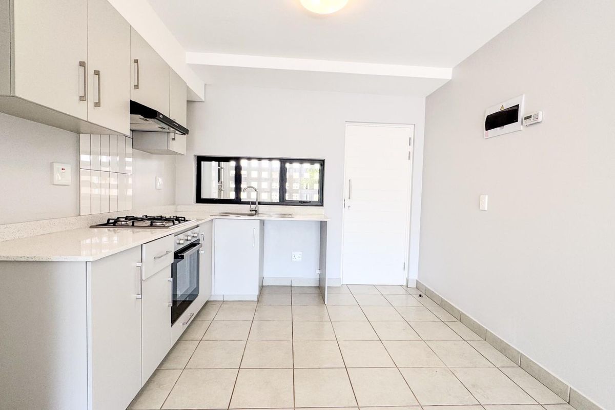 A clean, modern kitchen featuring light-toned cabinetry, a gas hob, built-in oven, and tiled flooring, offering a functional and bright workspace.