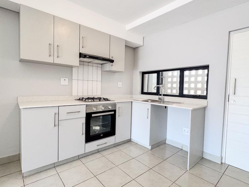 A clean, modern kitchen featuring light-toned cabinetry, stone countertops, a gas hob, built-in oven, and tiled flooring in a well-maintained apartment.