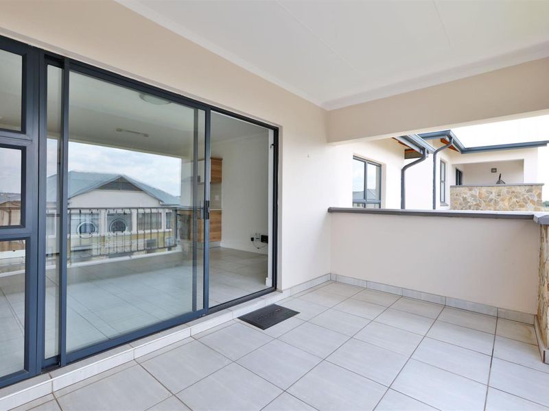A clean, covered balcony featuring tiled flooring, stone cladding accents, and large sliding glass doors providing access to the interior living space.