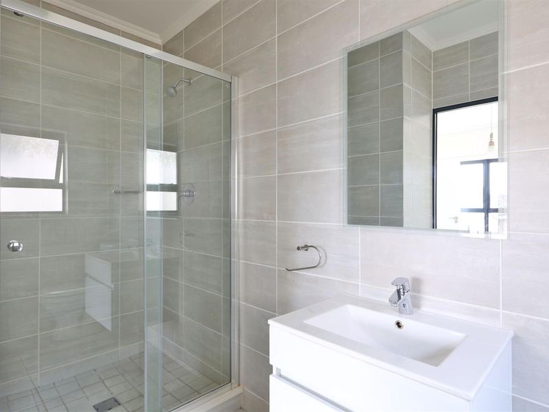 Modern bathroom featuring a glass-enclosed shower, a sleek vanity basin with a mixer tap, and neutral wall tiling.