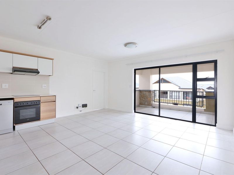 Bright open-plan living area featuring a modern kitchen with built-in appliances, tiled floors, and large sliding doors leading to a private balcony.