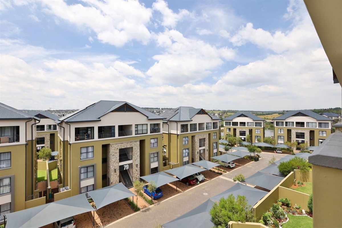 An elevated aerial view of a modern apartment complex featuring multiple residential blocks, paved driveways, and covered parking structures.
