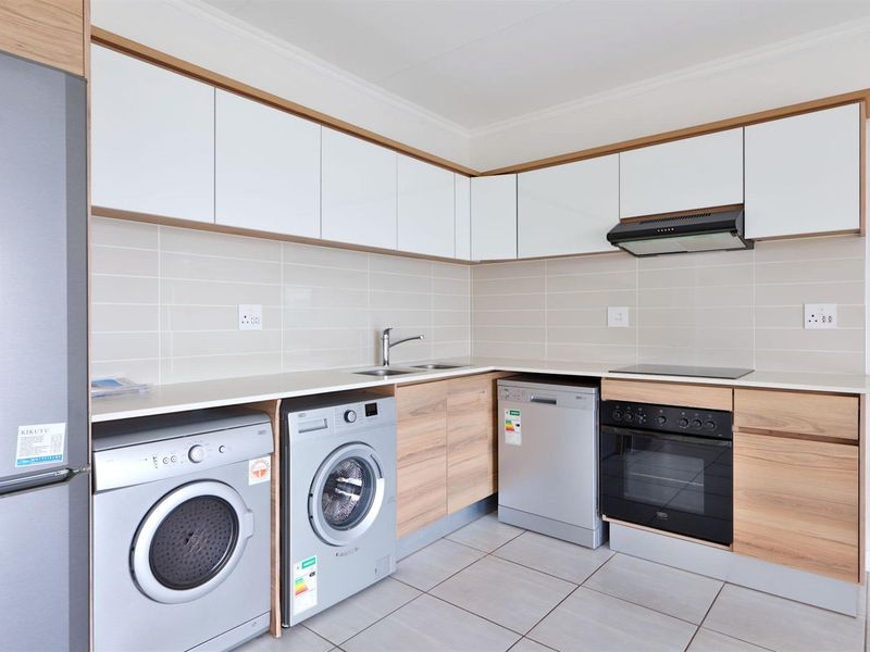 Modern kitchen featuring sleek white and wood-grain cabinetry, stone countertops, integrated oven, hob, extractor fan, and tiled backsplash with neutral floor tiles.