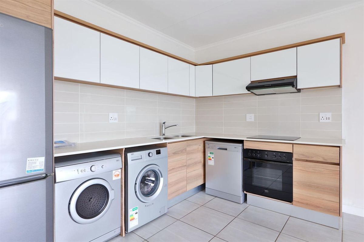 Modern kitchen featuring sleek white and wood-grain cabinetry, stone countertops, integrated oven, hob, extractor fan, and tiled backsplash with neutral floor tiles.