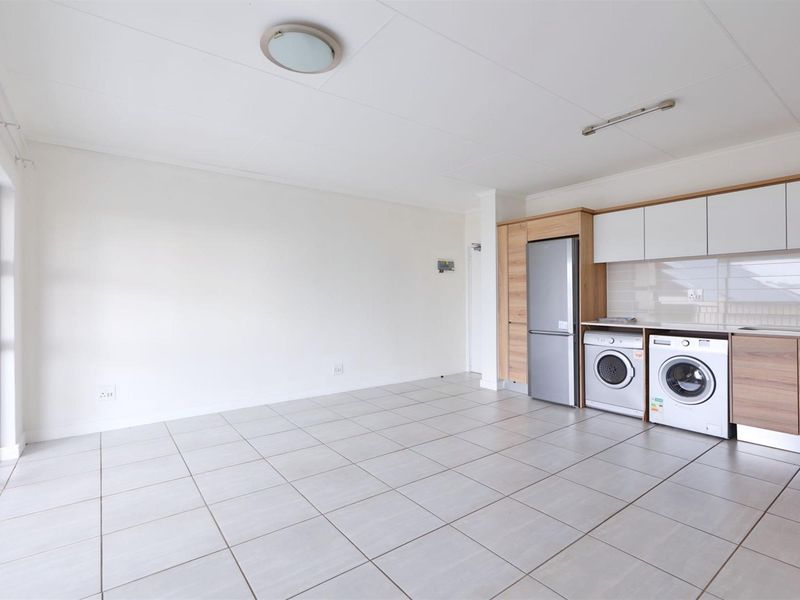 An open-plan living and kitchen area featuring tiled flooring, modern built-in cabinetry, and integrated laundry appliance connections.
