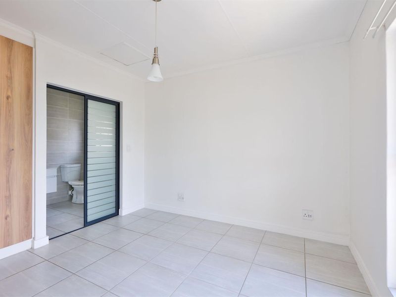 A bright, empty bedroom featuring tiled flooring, a built-in wardrobe, and an en-suite bathroom accessible via a modern sliding door.