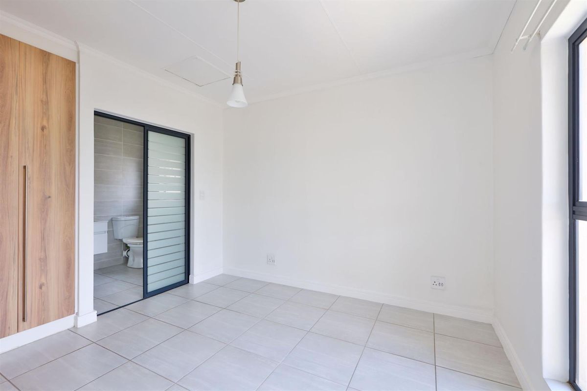 A bright, empty bedroom featuring tiled flooring, a built-in wardrobe, and an en-suite bathroom accessible via a modern sliding door.
