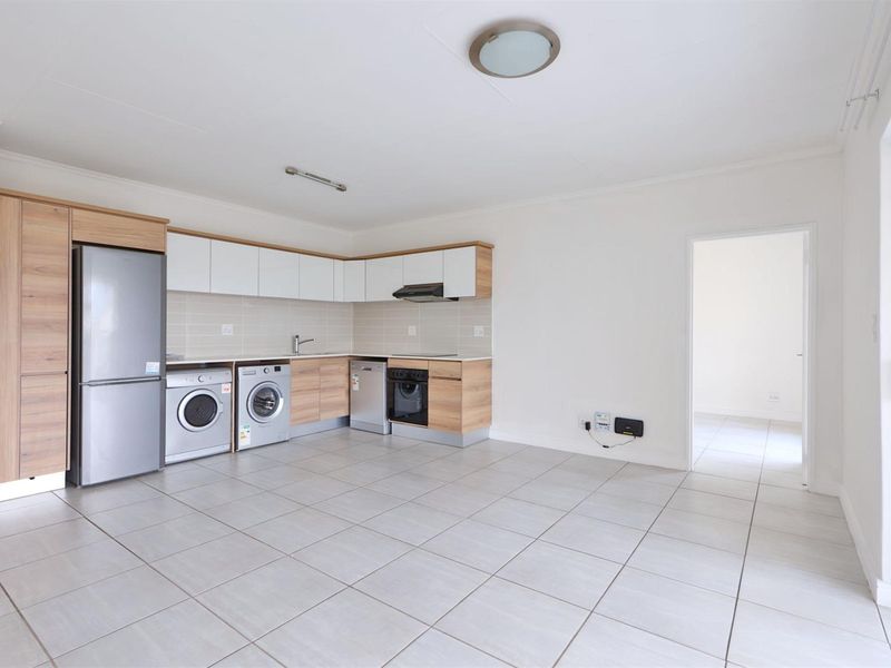 Modern open-plan kitchen featuring light wood and white cabinetry, tiled flooring, and integrated appliances, creating a clean and functional living space.
