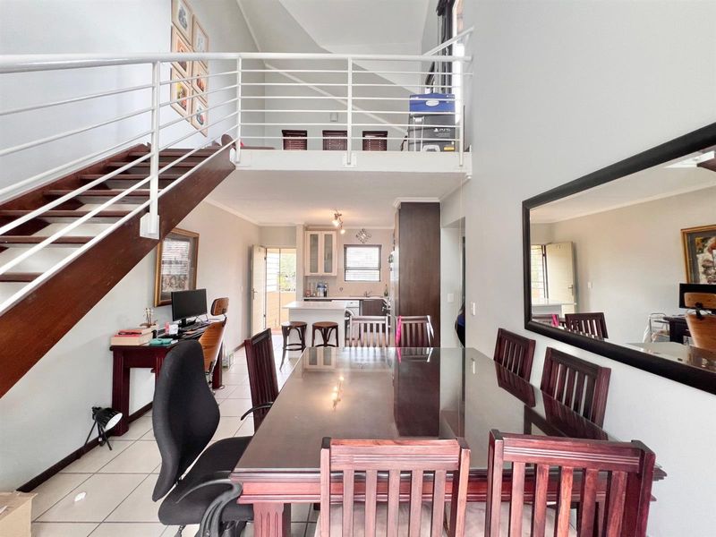 Open plan living and dining area featuring a mezzanine level, staircase, and a functional kitchen with island, offering a spacious and versatile layout.
