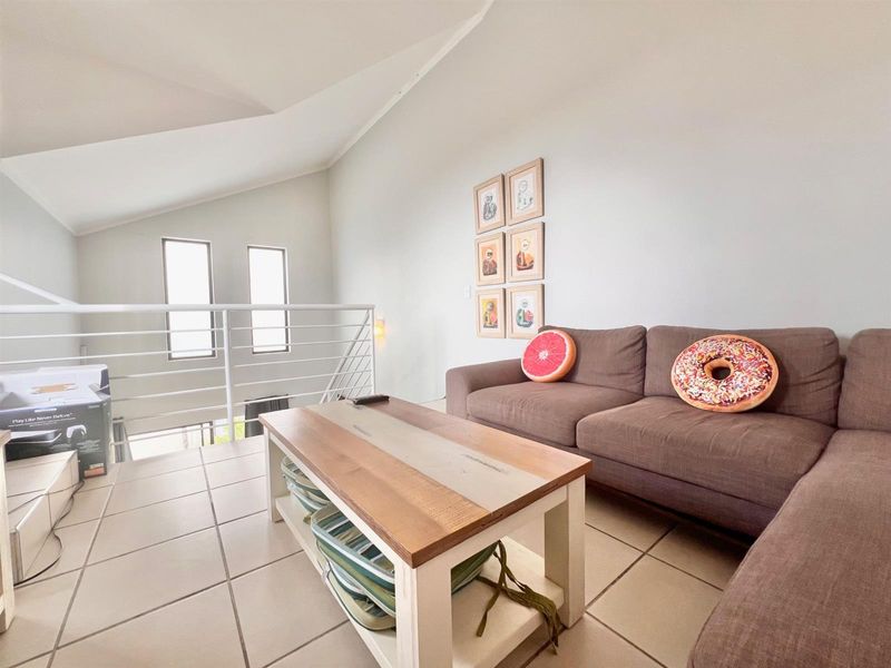A bright living area featuring tiled flooring, a vaulted ceiling, and a modern metal balustrade overlooking the lower level.