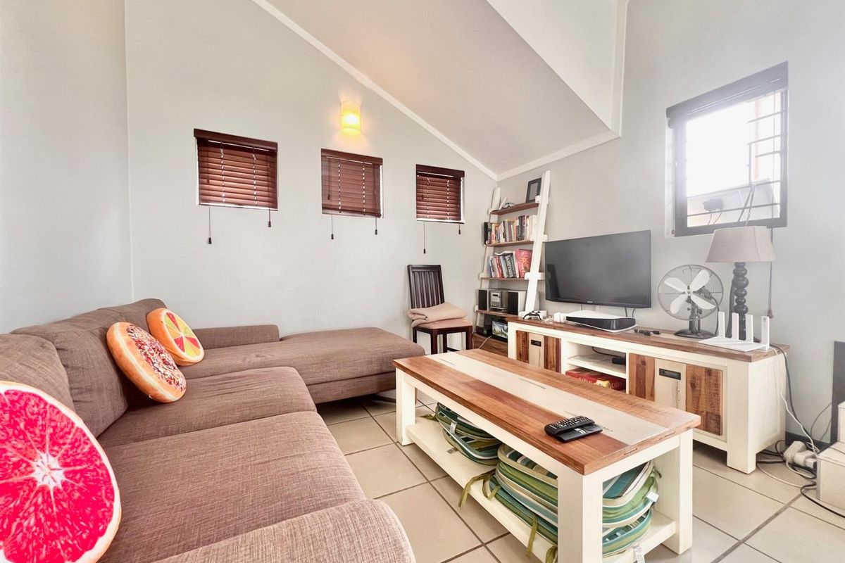A cozy living room featuring tiled flooring, a vaulted ceiling, and natural light through multiple windows with venetian blinds.