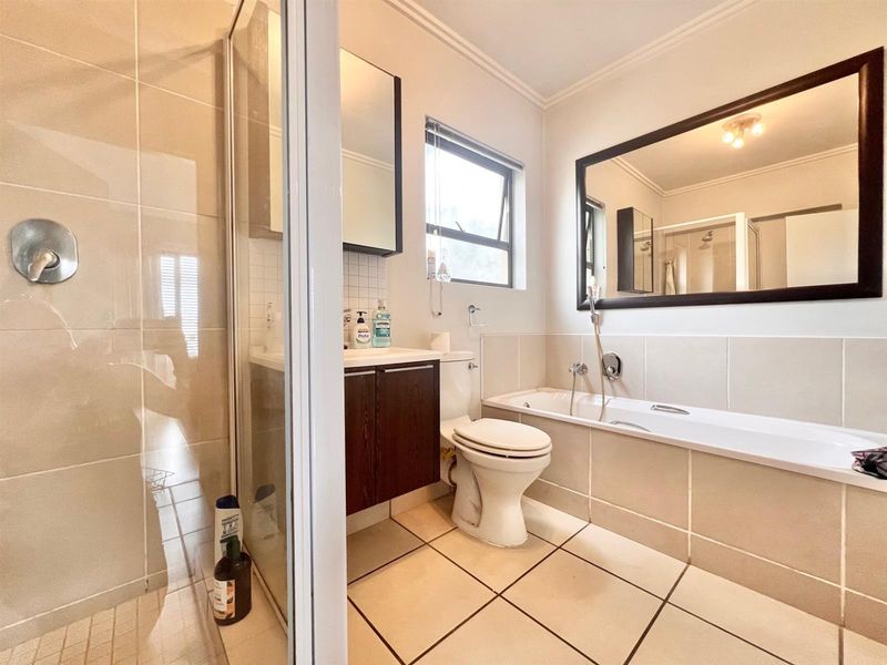 A well-maintained bathroom featuring a separate shower enclosure, bathtub, vanity cabinet, and neutral wall and floor tiling.